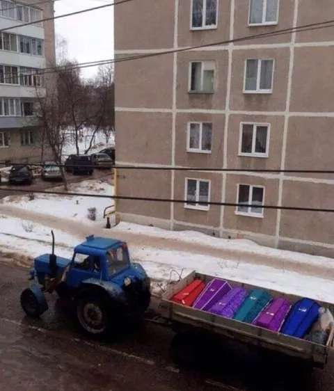 Трактор везёт разноцветные гробы