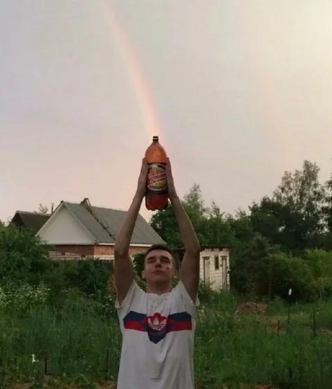 Парень поднимает бутылку к радуге