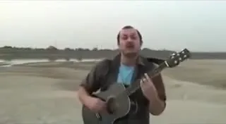 Мужчина поёт с гитарой на берегу