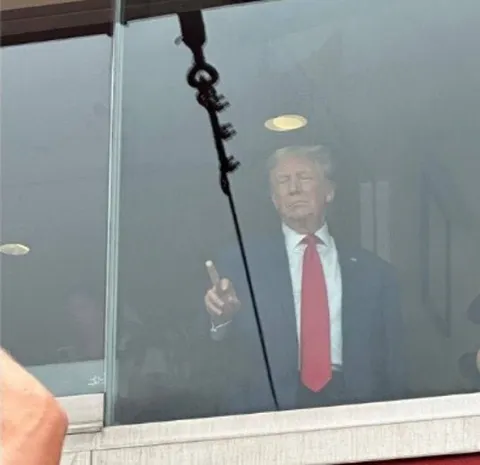 Трамп за стеклом показывает пальцем
